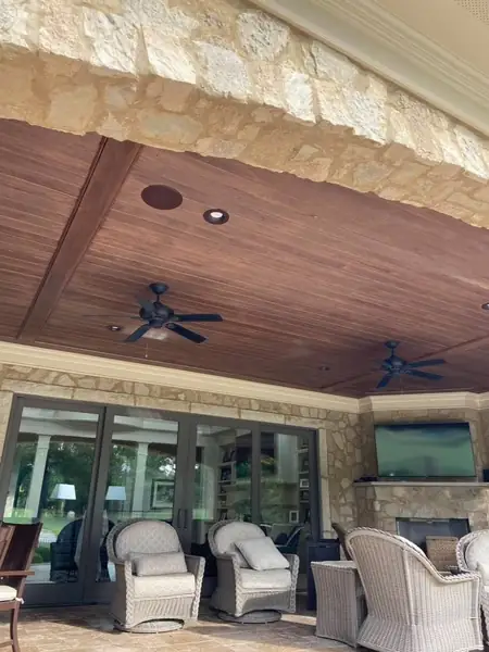 Stained tongue-and-groove porch ceiling with ceiling fans and stone arch