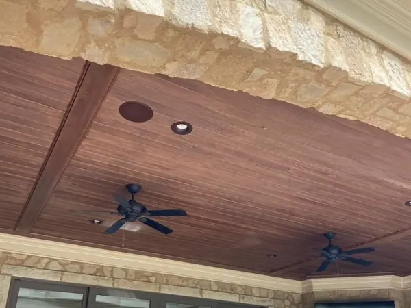 Stained tongue-and-groove porch ceiling with a wood beam under a stone arch